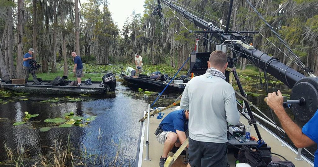 A film crew works in a swampy location.
